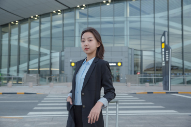 一位身穿正装的女白领站在航站楼外带着行李看向镜头