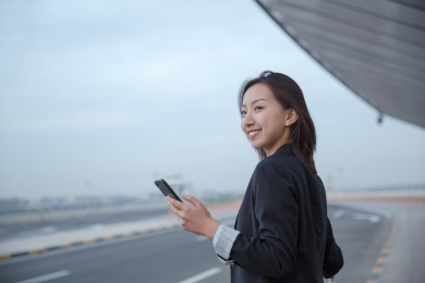 一位手拿之恩能手机的女白领站在路边手拿智能手机