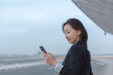 一位商务女士手拿智能手机站在路边