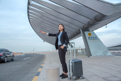 一位商务女士站在路边伸手打车边上放这一个行李箱