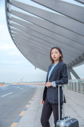 一位商务女士在路边等车边上放着拉杆箱