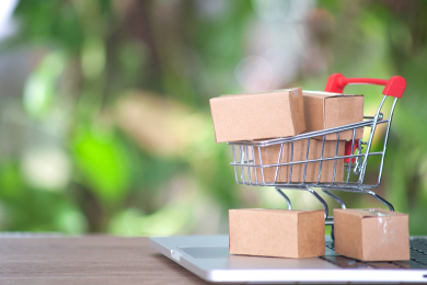 打开的笔记本电脑键盘上一辆满载快递包裹的购物车