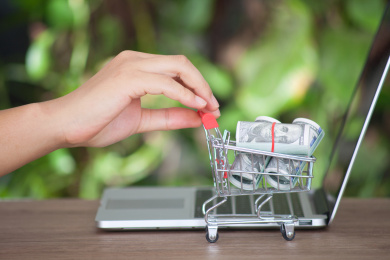 手推笔记本电脑旁满载美元钞票的购物车