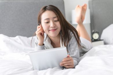 一名年轻女性趴在床上使用平板电脑看电影