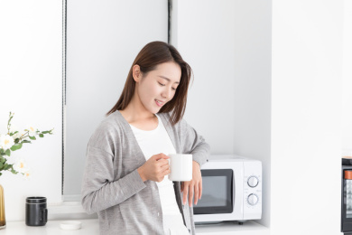 一名年轻女性站在厨房拿着水杯休息