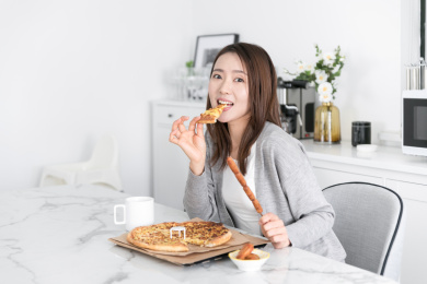 一名年轻女性在餐桌上吃拿着烤串吃披萨