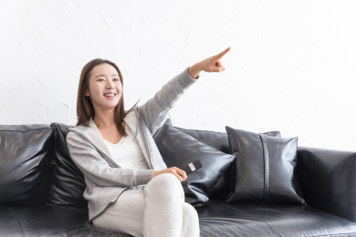 一名年轻女性在沙发上指着电视微笑