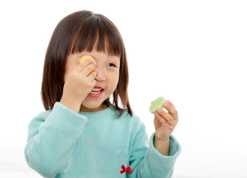 手拿着马卡龙贴在眼睛上玩耍的小女孩