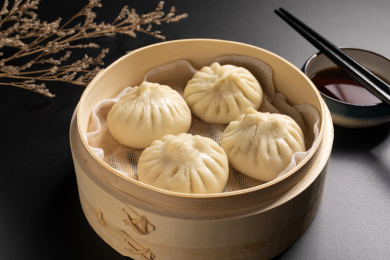 蒸笼里盛放着包子摆放在黑色背景上旁边摆放醋碟筷子