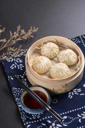 蒸笼里盛放着包子摆放在黑色背景上旁边摆放醋碟筷子