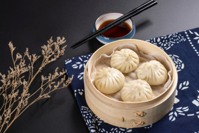 蒸笼里盛放着包子摆放在黑色背景上旁边摆放醋碟筷子