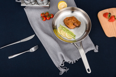 一只装有猪排和芦笋柠檬片不锈铁钢剪锅放在桌面上