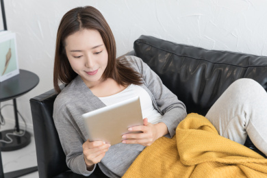 一名年轻女性靠在沙发上玩平板电脑