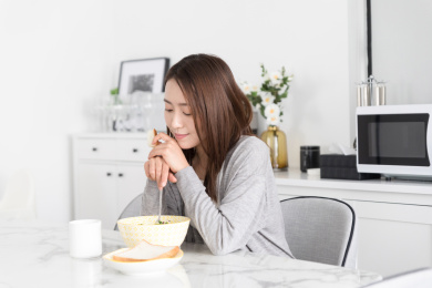 一名年轻女性在家里的厨房低头吃饭