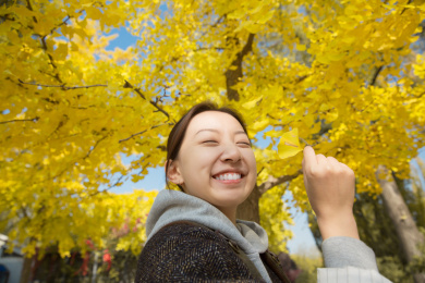秋天站在银杏树下的年轻美丽的中国女孩