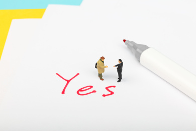 两个西装男性站在红色的yes旁握手