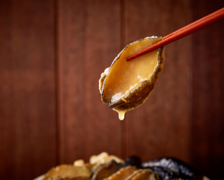 木纹背景中木质筷子夹起的鲍鱼特写