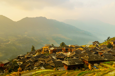 中国贵州黔东南加榜加车村秋季金黄色梯田中的吊脚楼远景