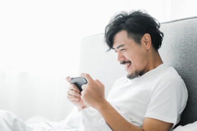 年轻男人坐在床上玩手机游戏