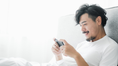 年轻男人坐在床上玩手机游戏