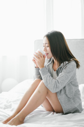 年轻漂亮的女性坐在床上喝水