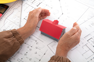 一双老年人的手呵护着平面图纸上的一个小房子模型