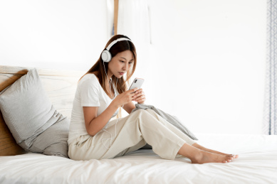 一位年轻女性在床上一边使用手机一边听音乐