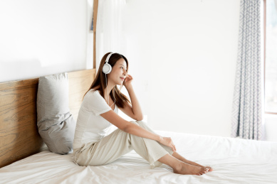 一位年轻女性在床戴着耳机享受音乐
