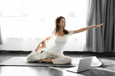 一位年轻女性在卧室使用电脑学习瑜伽