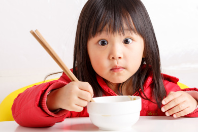 饭桌上拿筷子吃饭的小女孩