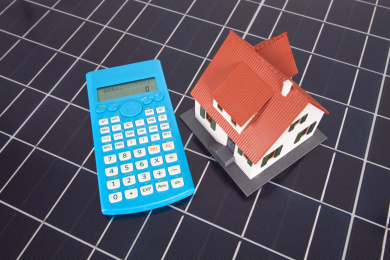 太阳能板背景上的计算器和小房子模型