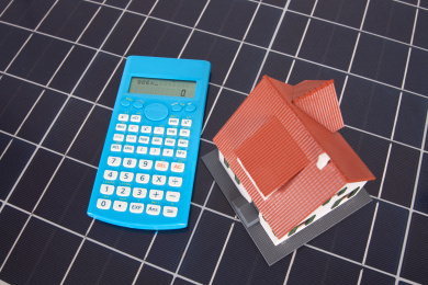 太阳能板背景上的计算器和小房子模型