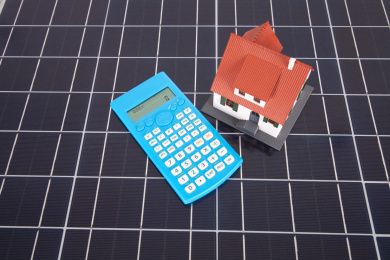 太阳能板背景上的计算器和小房子模型