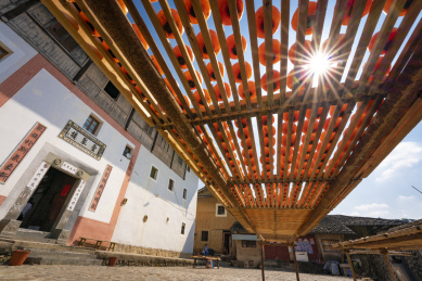 方形土楼前太阳光透过曝晒在竹盘里的柿子形成星芒，中国福建永定