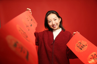 拿着新年春联穿着红色外套的中国女孩站在红色背景墙前