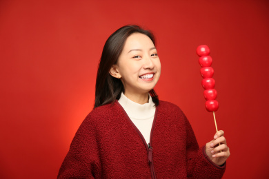身穿红色外套的美丽女孩手里拿了一串糖葫芦站在红色背景墙前