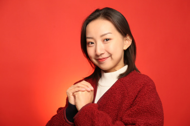 穿着红色外套站在红色背景前双手抱拳拜年的年轻女孩