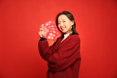 手里拿着一叠红包的中国女孩站在红色背景墙前