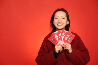 双手捧着一堆红包的可爱女孩站在红色背景墙前开心大笑