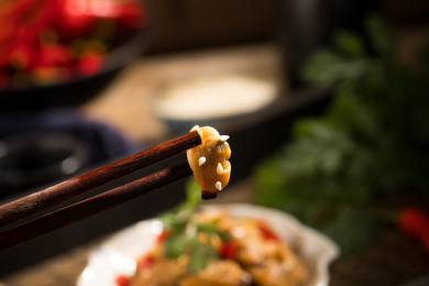 筷子夹着一个粘有白芝麻的蛤蜊肉