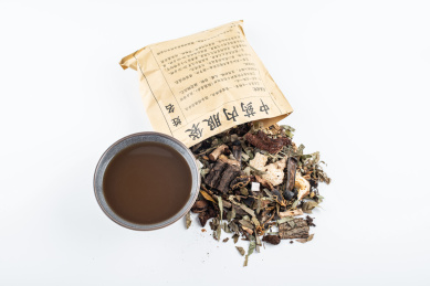 白背景上一纸袋中药材和一碗熬煮好的药汤