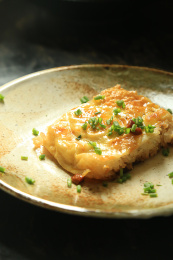 黑背景上黄褐色盘子中的一块三鲜豆皮，上面撒着葱花