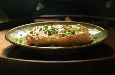 托盘上黄褐色盘子中的一块三鲜豆皮，上面撒着葱花