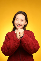 站在黄色背景前双手抱拳拜年的年轻女人