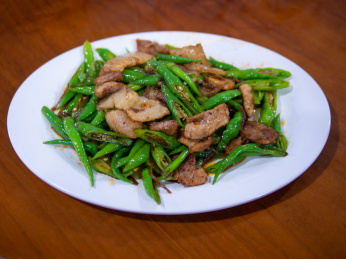 木桌上白色餐盘里的一盘中国特色川菜尖椒回锅肉