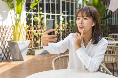 坐在室外咖啡桌前手机视屏通话的商务女青年