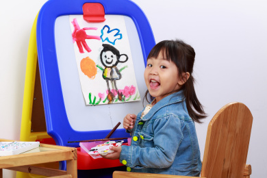 小女孩手拿水彩笔在画架上涂鸦画画