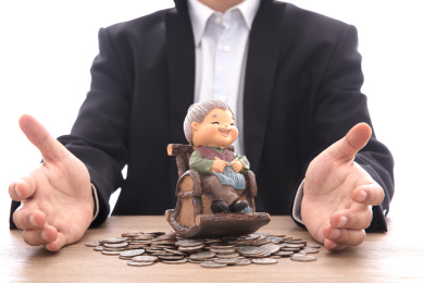 身穿黑西服的男士双手呵护着一个放在硬币上的老奶奶模型