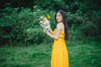 穿黄裙子手拿鲜花站在草坪上的女孩