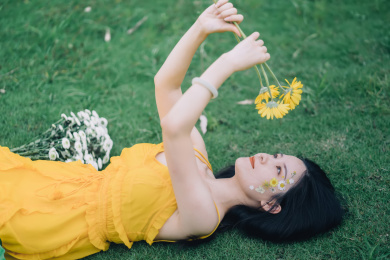 穿黄裙子手捧鲜花躺在草坪上的美丽女孩人像